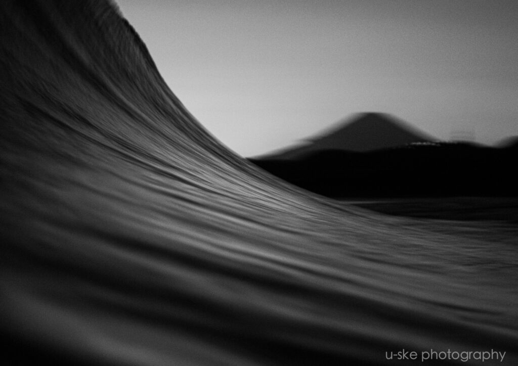 流れる波と夕焼けに浮かぶ富士山のシルエットを捉えたモノクロ写真